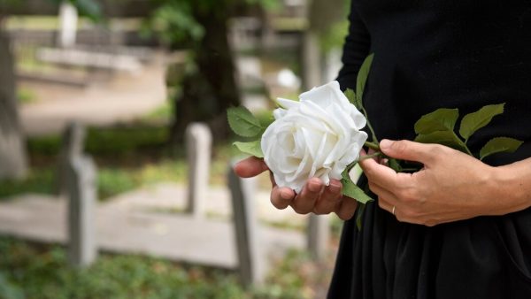 Una mujer sostiene una rosa blanca en un cementerio
